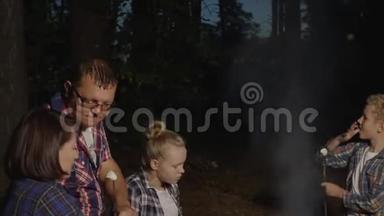 一家人在<strong>夏日</strong>森林的篝火上吃着热的棉花糖。<strong><strong>旅</strong>游</strong>家庭在森林里品尝烤棉花糖