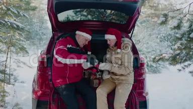 一对戴着圣诞帽的幸福夫妇在冬林里从汽车后座的<strong>保温</strong>瓶里喝着热茶。红衣男女