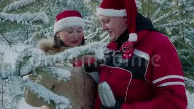 一对戴着红色圣诞帽的浪漫情侣在雪林里<strong>喝</strong>着<strong>热水</strong>瓶里的热茶。爱<strong>喝</strong>酒的男女