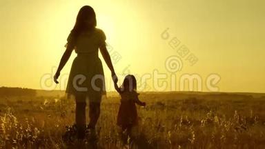 小<strong>女儿</strong>和妈妈牵着手在田野里走来走去。 宝贝牵着妈妈`手。 幸福的<strong>一家人</strong>傍晚走出家门