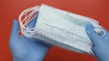 医生在红色背景下用<strong>蓝色</strong>医用手套保护<strong>手中</strong>的抗病毒口罩。