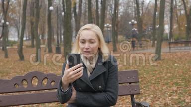 女博主坐在一个荒无人烟的秋天公园的长椅上，在视频聊天上聊天.. 流感大爆发的人