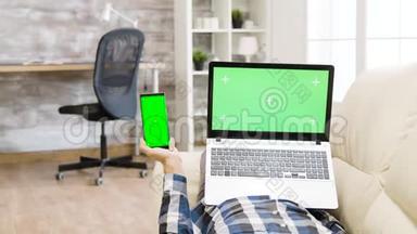 视差镜头：躺在沙发上，手里拿着一部绿色屏幕智能手机和笔记本电脑