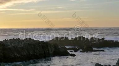 在太平洋格罗夫(Pacific Grove)日落的天空下，在多岩石的海岸上，一波一波缓慢移动的泛右太平洋海浪在翻滚和破碎