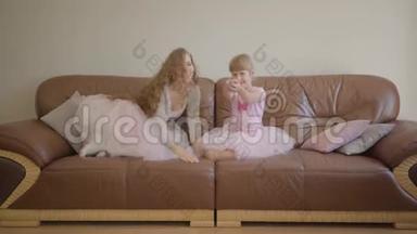 快乐的白种人妈妈和女儿穿着同样的粉红色连衣裙跳上教练，用<strong>遥控器</strong>转动<strong>电视</strong>