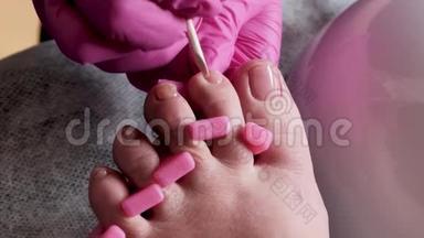 带粉色手套的教育学大师是用钻头在修脚沙龙切割角质层和紫胶脚趾甲。