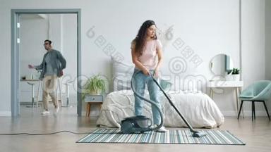 家庭主妇用吸尘器打扫地板，而戴耳机的男人则在卧室里跳舞