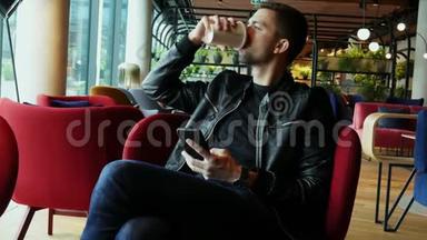 迷人的男人在现代时尚的咖啡馆里喝咖啡，用手机浏览互联网