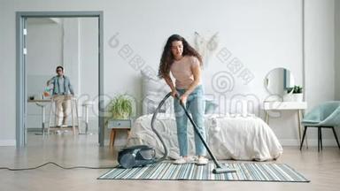 年轻女子用吸尘器清理地毯，而男子则用耳机清理家具