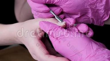 美甲师傅在粉红色手套上用电钻刮掉美甲沙龙的旧清漆。 专业修指甲