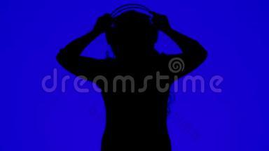 一位女士戴着耳机，在蓝色背景下随着音乐起舞的剪影