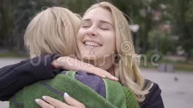 两个高加索女朋友拥抱，他们很高兴见到对方。 女人在街上相遇。 相聚的真诚喜悦