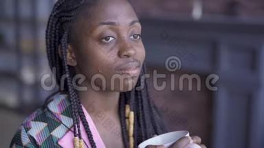 体贴的非裔美国女人，带着一杯茶或咖啡<strong>看</strong>着<strong>远方</strong>。 有皮肤问题的女孩在家休息