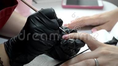戴黑色手套的指甲油师傅在指甲上涂粉红色指甲油