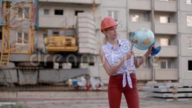 <strong>小巧可爱</strong>的年轻女子戴着建筑头盔，手里拿着地球仪，可调节的扳手指向乡村或城市