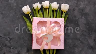白色郁金香花与粉红色礼品盒在深灰色背景平躺。 4K视频