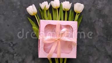 白色郁金香花与粉红色礼品盒在深灰色背景平躺。 4K视频