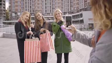 三个带着购物袋的快乐女孩摆姿势给第四个朋友拍照。 城里四个时尚女人