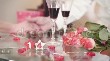 玻璃桌上摆着一束玫瑰和酒杯。 成熟的男人用手掌`高级妻子