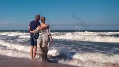 一对苗条的夫妇，一个穿着牛仔短裤的男人和一个穿着漂亮长裙的女人站在沙滩上的<strong>大风</strong>中