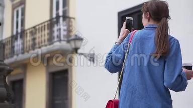 时尚的年轻<strong>游客</strong>手里拿着一杯咖啡，在电话里拍下了当地一个<strong>景点</strong>的照片。