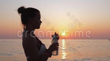 女孩在日落时在海边或海边喝水。
