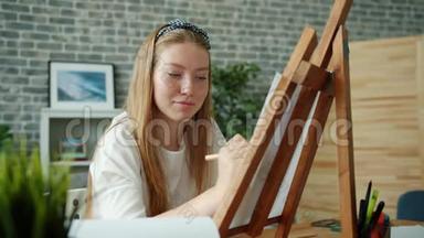 幸福的年轻女士坐在画架上用彩色铅笔在家<strong>画画</strong>画