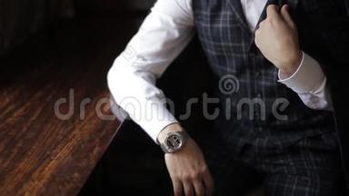 一个优雅整洁的男人，带着一只银色手表和一套昂贵的格子西装的近景。 穿格子花格子的时髦富有的新郎