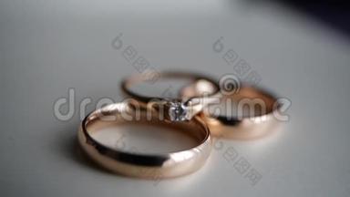 三个漂亮的金戒指-一个订婚钻石和一个结婚戒指躺在一张白色的桌子上。 礼物和浪漫