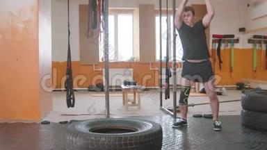 <strong>室内运动</strong>训练-一名带保护膝垫的男子在健身房用金属锤击一个大轮胎