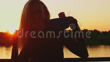 一位美丽的金发女郎手持一块小滑板在河边的夕阳下摆姿势