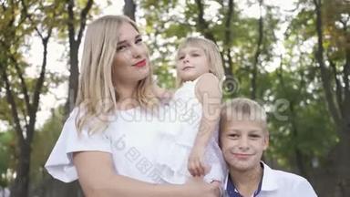 漂亮的金发女人抱着小女儿，大儿子抱着妈妈微笑。 快乐的肖像