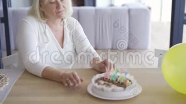 伤心的、不快乐的、成熟的女人坐在EMLPY房间的小生日蛋糕前的桌子旁，然后站起来走着