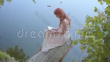 年轻迷人的女孩，一头红色的长发，穿着<strong>淡粉</strong>色的连衣裙，正在蓝色湖畔读诗。 吸引力