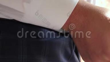 穿白衬衫的商人把腰带系在裤子上。 特写镜头。 男人早上穿衣服上班。 办公室职员