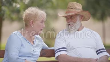 老白种人夫妇坐在<strong>夏季</strong>公园的长凳上聊天。 戴草帽的成熟<strong>男</strong>人