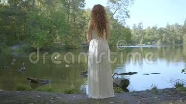 后景<strong>美丽</strong>苗条的女人，红色的头发，穿着白色的长裙，站在河岸上看着远处。 <strong>美丽美丽</strong>