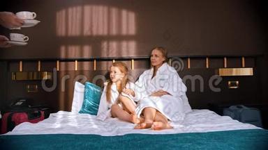 <strong>一家人</strong>在酒店房间里穿着白色浴袍-爸爸把茶杯带到床上给他的妻子和<strong>女儿</strong>