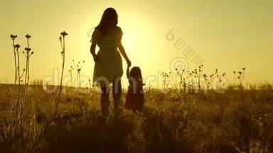 小<strong>女儿</strong>和妈妈牵着手在田野里走来走去。 宝贝牵着妈妈`手。 幸福的<strong>一家人</strong>傍晚走出家门
