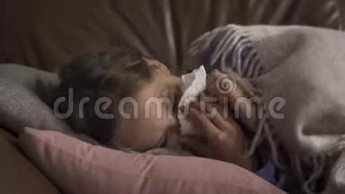 一个生病的年轻白种人女孩在家里躺在毯子下<strong>咳嗽</strong>和吹鼻子。 孩子发烧了