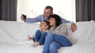 幸福的家庭一<strong>起坐</strong>在沙发上。 一位父亲给他的妻子和儿子拍自拍照片。 技术