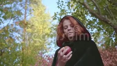 一个穿着黑色长袍的红发白种人女人的特写镜头看着她<strong>手中</strong>的苹果。 仙女站着