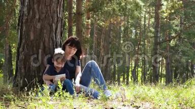 一位年轻的母亲和她的儿子正在公园里放松，坐在一棵树旁，用一个<strong>小</strong>玩意。 当代<strong>科技</strong>。