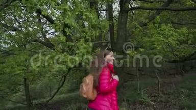 戴着太阳镜穿着红色夹克衫的微笑女孩来到大树附近的古老的木制楼梯，并测试它是否颤抖