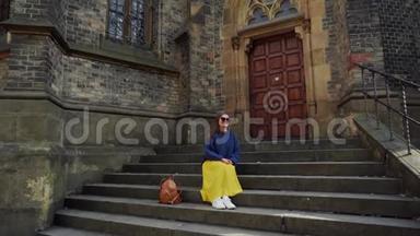 美丽的女孩穿着一条黄色长裙，背着背包坐在靠近<strong>天主教</strong>会的台阶上，总计划