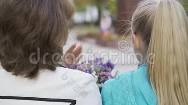 笑着的白种人不同年龄的妇女坐着一束野花和交谈。 奶奶在聊天
