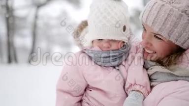 在雪天的圣诞节假期，妈妈带着女儿穿连身衣。 穿着粉色连衣裙和婴儿一起走路的女人
