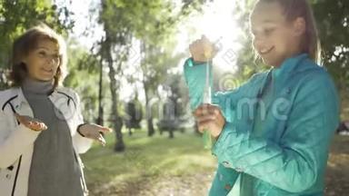 快乐的少年白种人女孩在阳光明媚的公园里玩肥皂泡。 孙女招待她年轻的容貌