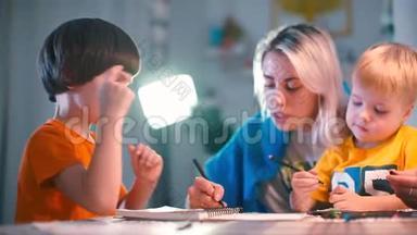 两个带老师的男孩在幼儿园的一张桌子上画纸。