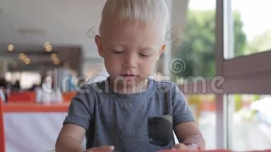 可爱的小男孩坐在街头咖啡馆看着电话。 坐在咖啡馆里用电话看动画片的漂亮孩子